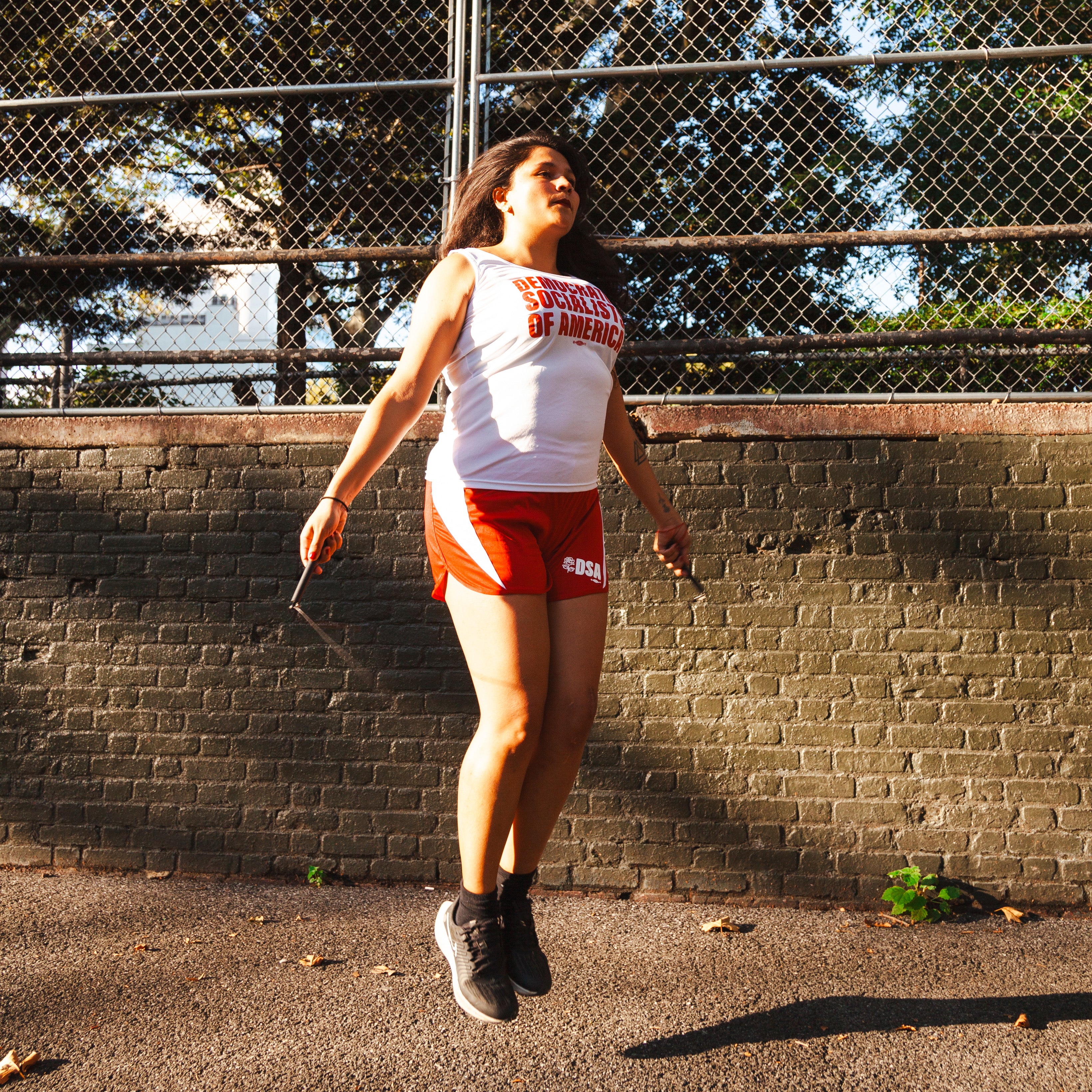 a socialist wearing a DEMOCRATIC SOCIALISTS OF AMERICA track uniform jumps rope in a public park