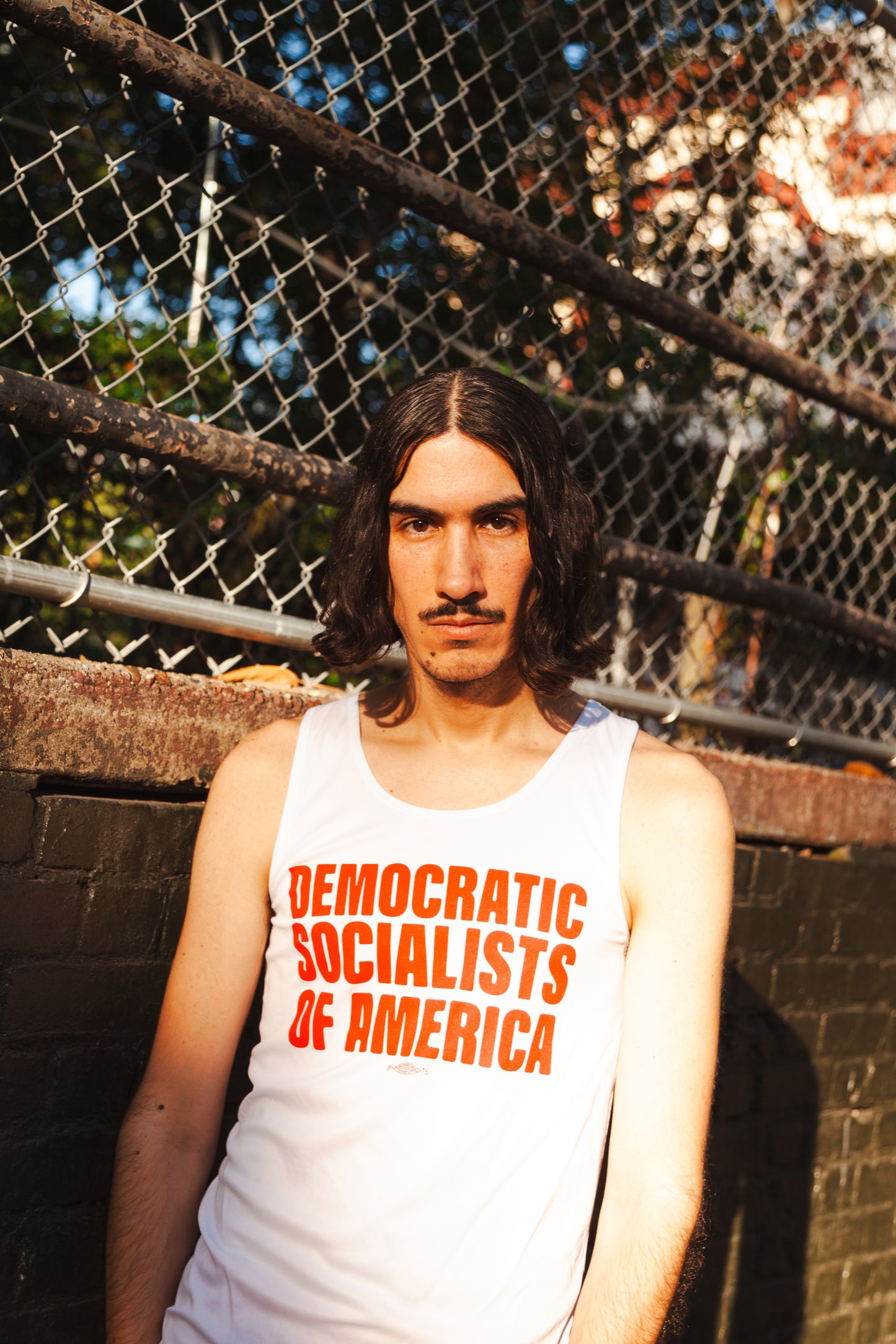 Socialist in a public park wearing a white tank top that says DEMOCRATIC SOCIALISTS OF AMERICA 