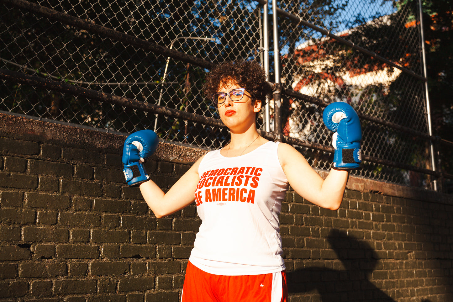 Socialist in track tank top poses with boxing gloves on a public athletic court.