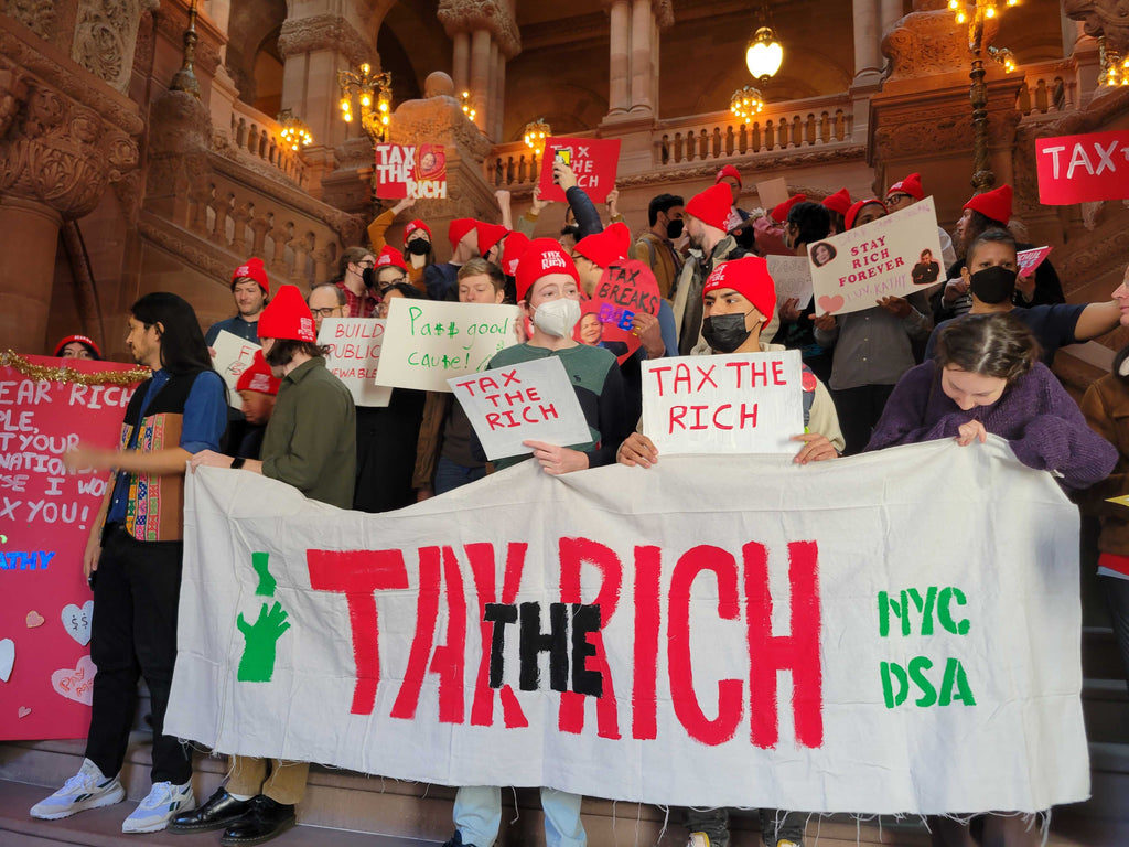 many socialists standing on the "million dollar staircase" in the Albany legislature, wearing Tax the Rich beanies